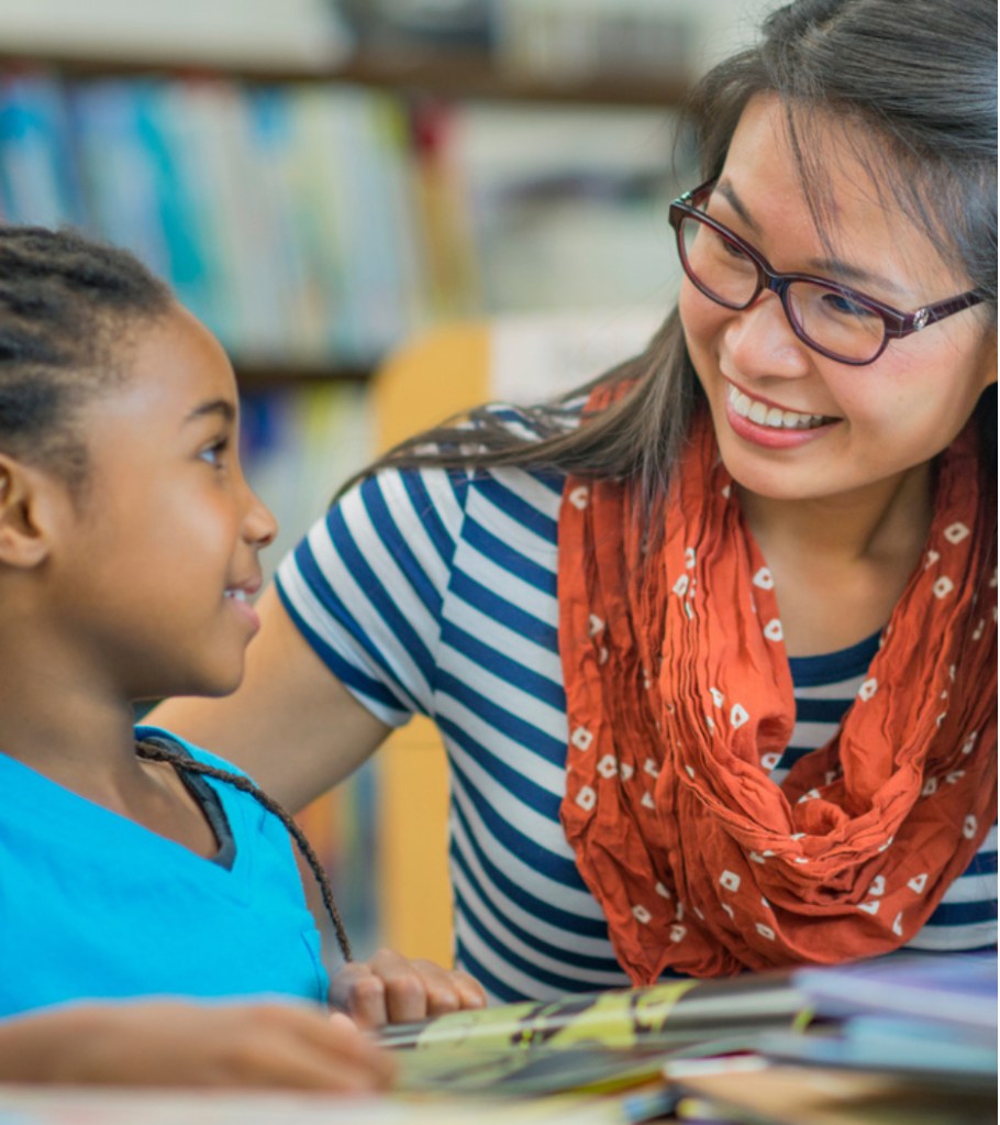 An adult reading a book with a child, sitting together and sharing a moment of learning and connection.