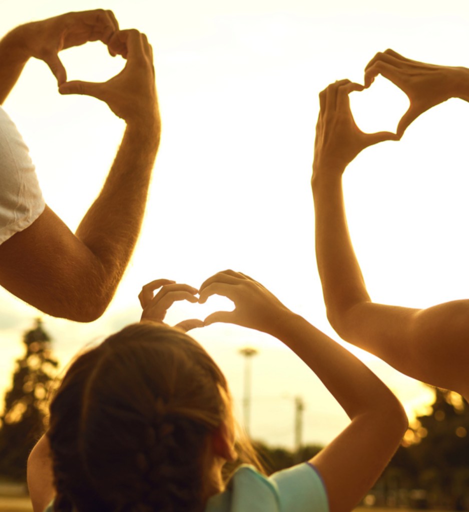 A family of three forming heart shapes with their hands.