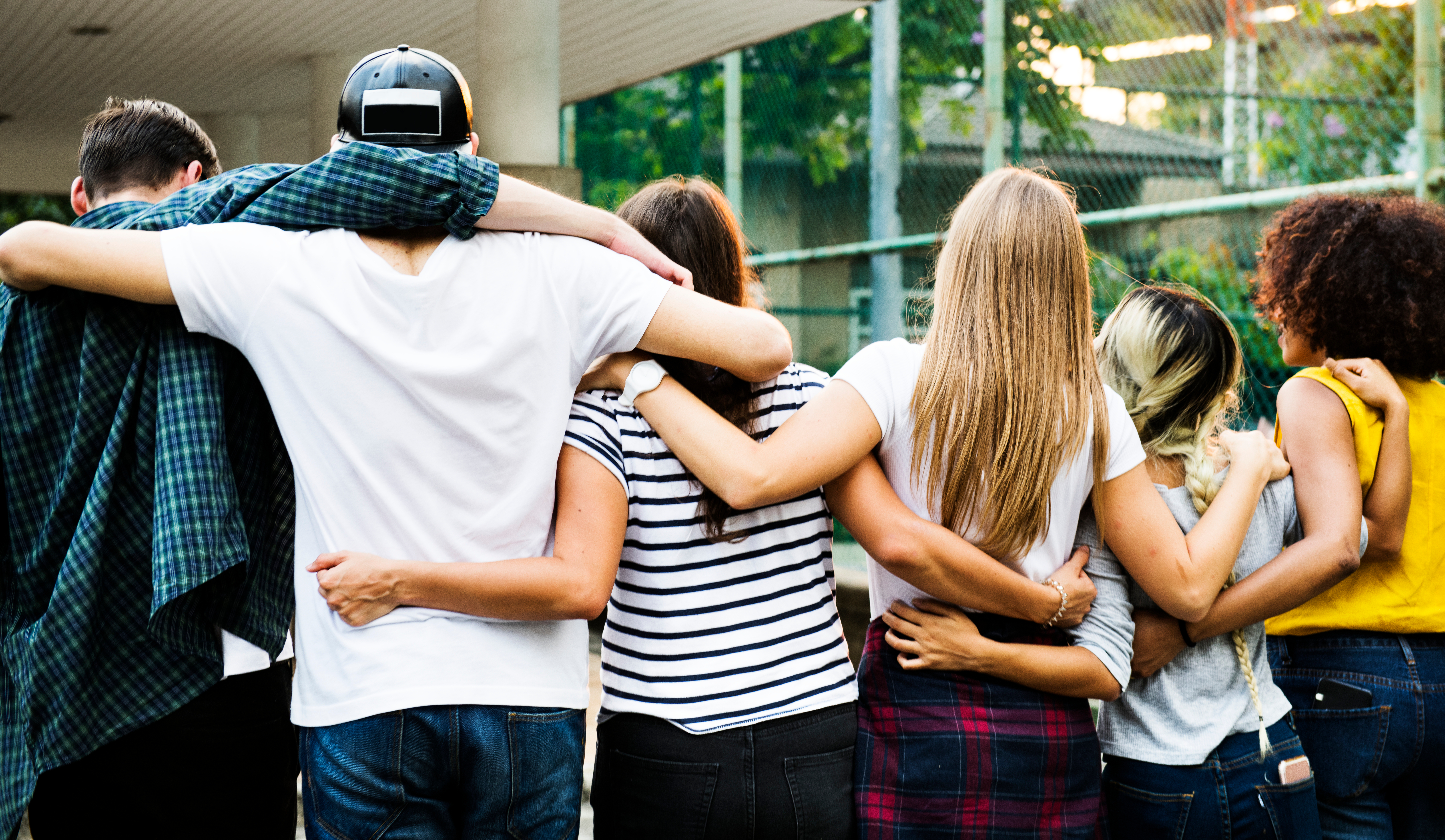 A group of teenagers standing together with their arms around each other, showing friendship, support, and connection.